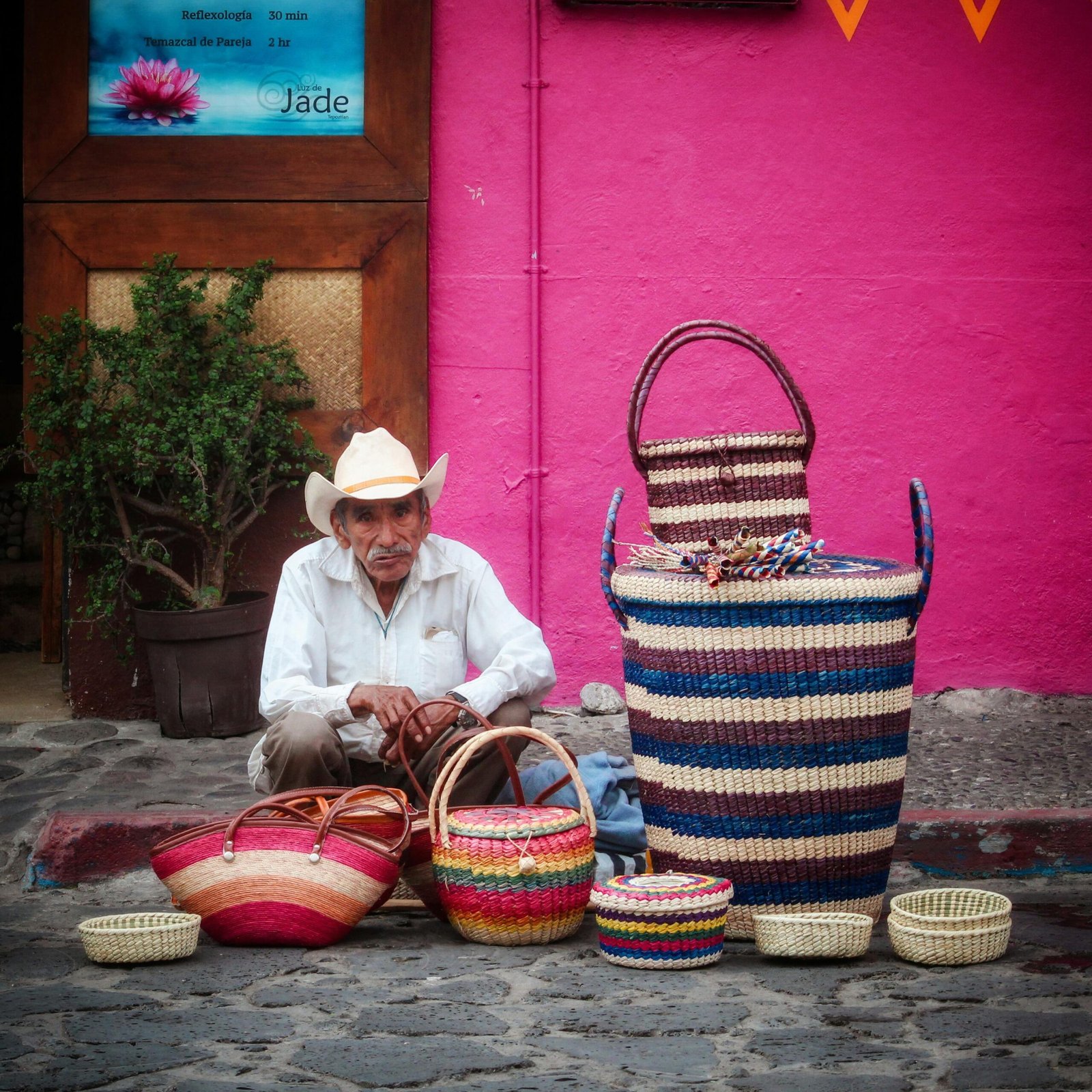 An elderly street vendor in Tepoztlán, Mexico, selling colorful handmade baskets on a vibrant street.